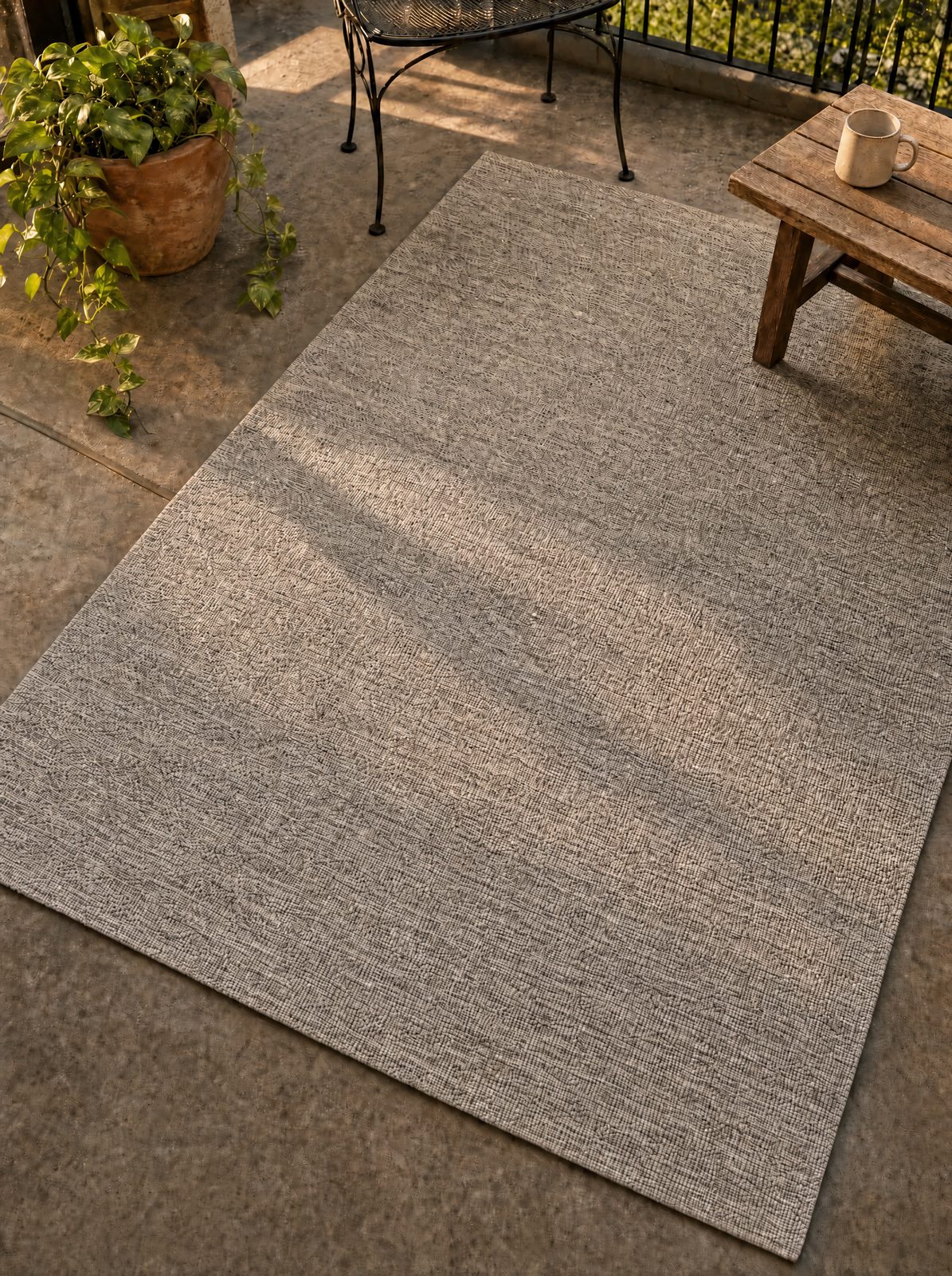 Unique Loom heathered beige 5x8 outdoor flatweave rug on a sunlit patio showing warm and cool tonal depth in the weave, two chairs and a potted plant on top